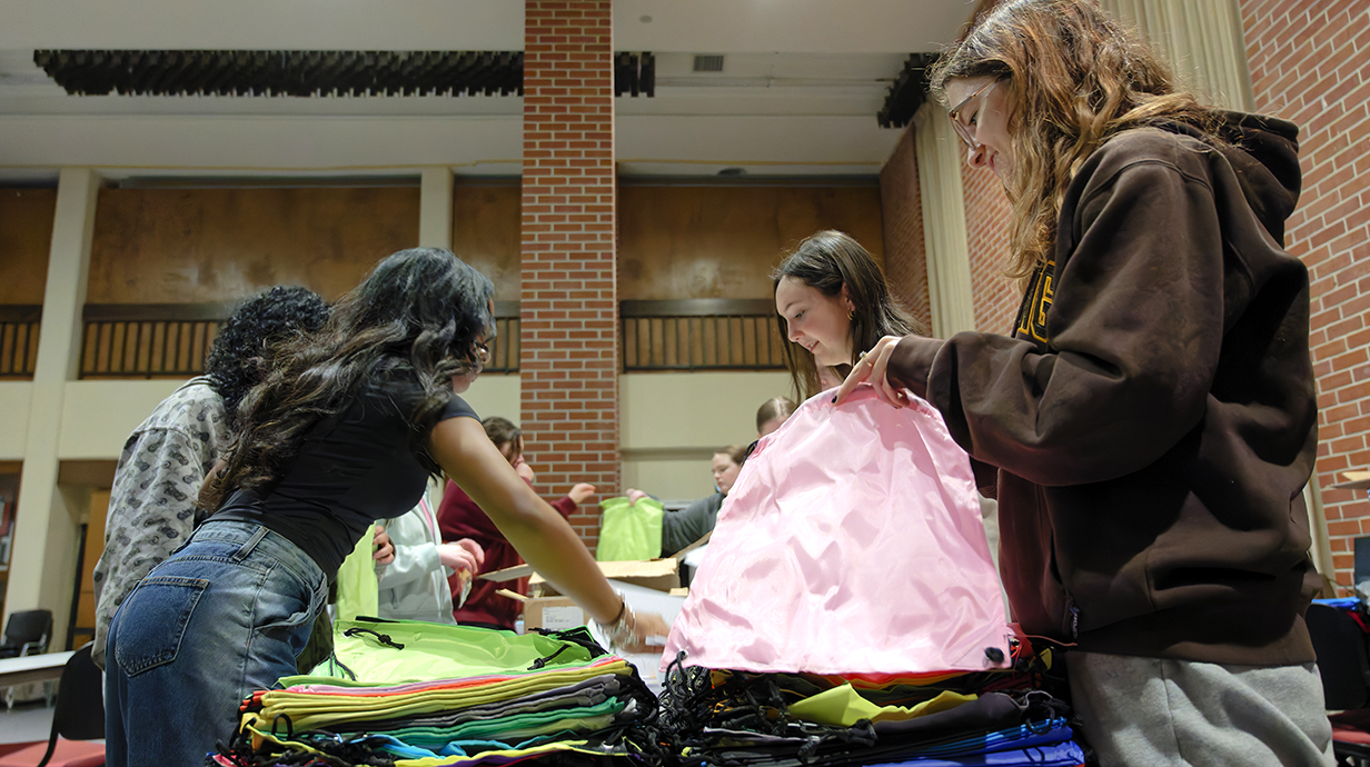 A group of young people pack items into colorful tote bags with drawstrings.