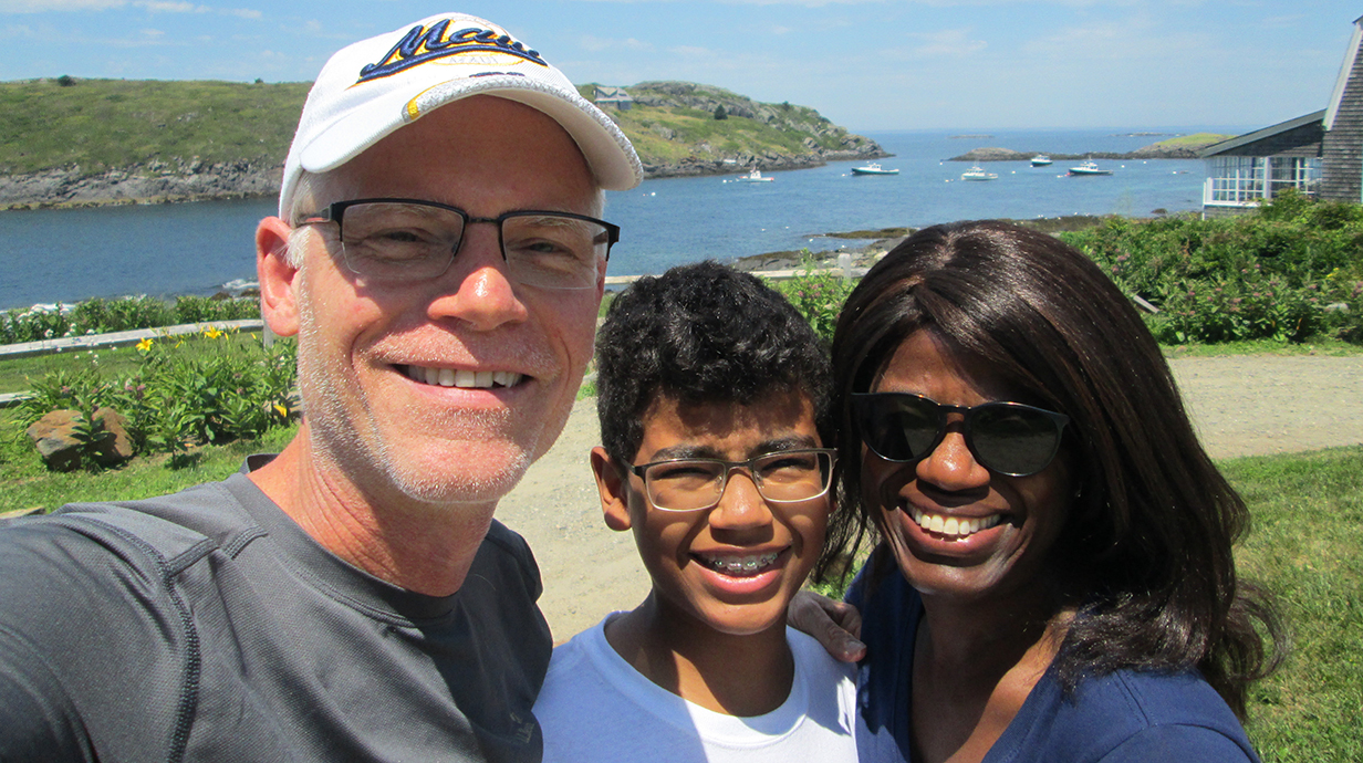 A man, a woman and a young boy take a selfie outdoors in front of a river.