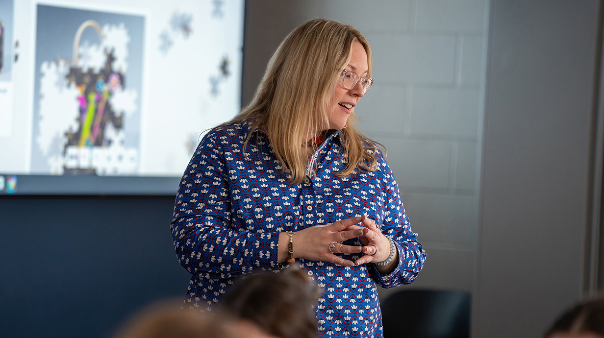 A teacher talks while standing in front of a projection screen in a classroom.