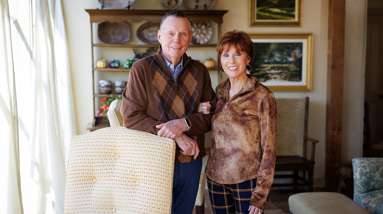 A man and woman stand for a portrait in a sunny living room.