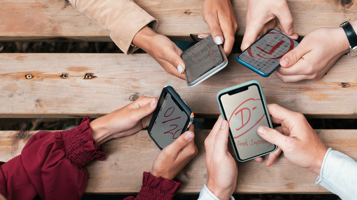 Four sets of hands around a table hold cellphones, all with grades marked on them.