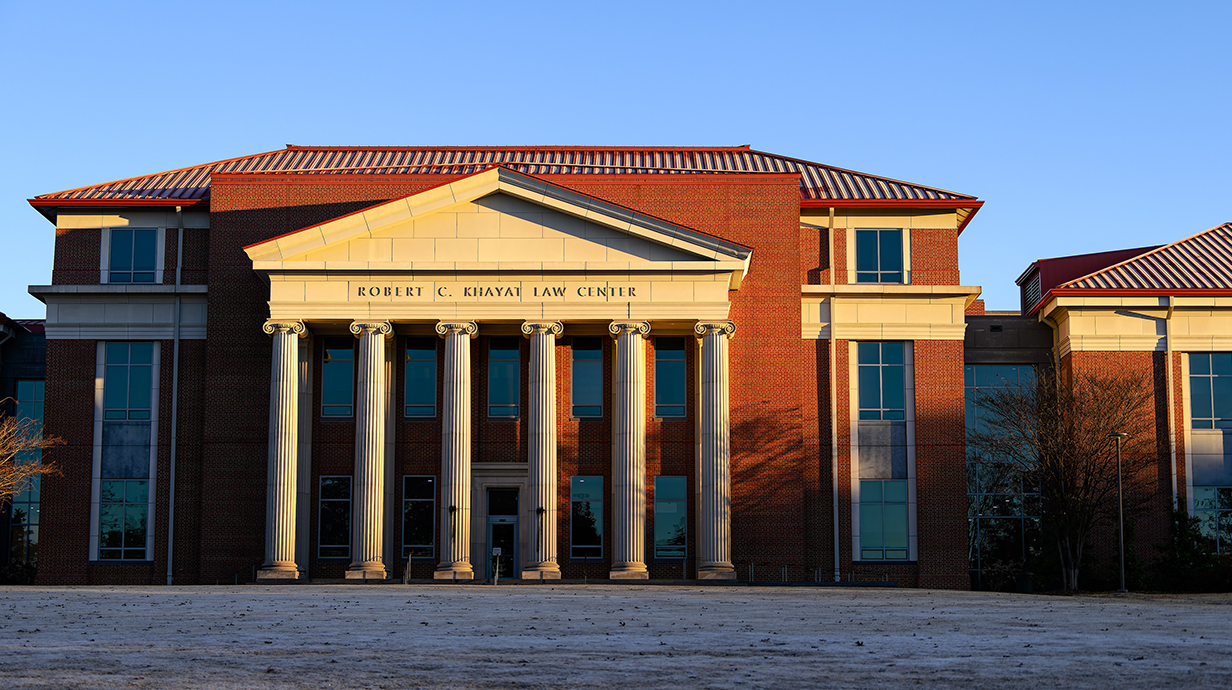 The early morning sun lights a large red brick building with white columns.