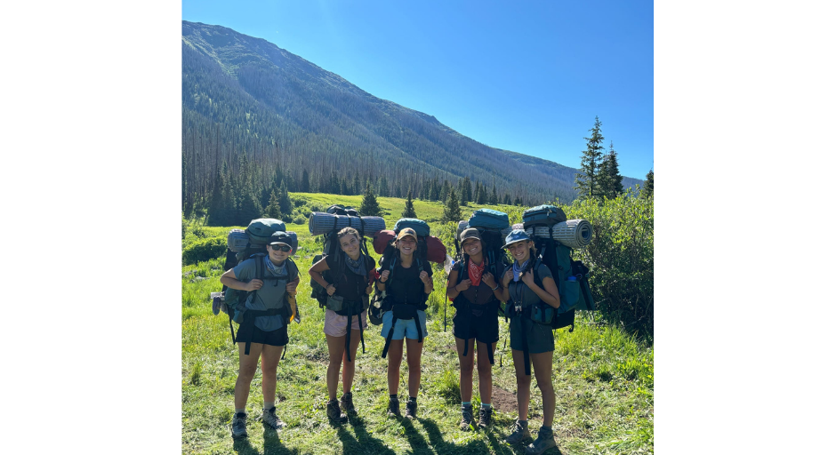 Sadie Keyes posing with four other girls, all with backpacks on, outside with a mountain and trees in the background.