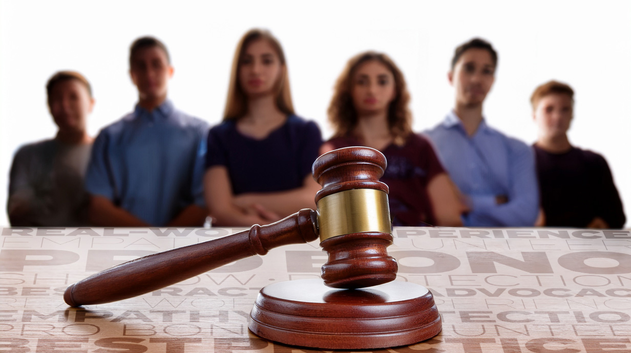 A close-up photo of a judge's gavel with a small group of young people gathered in the background.