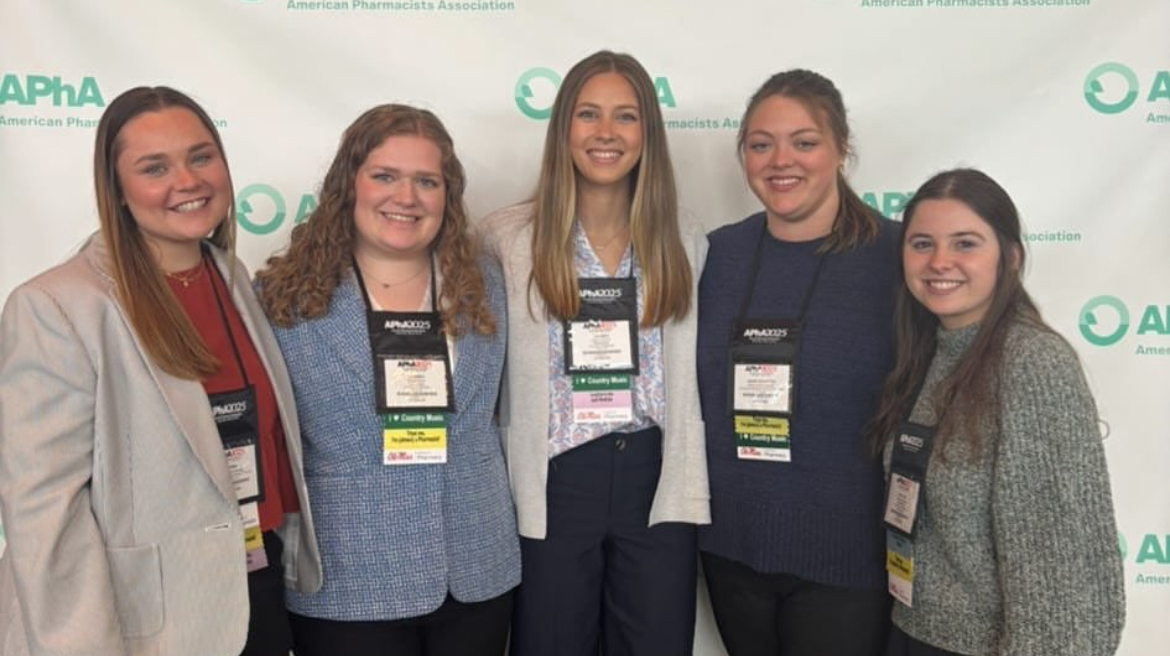 Five young women wearing nametags stand in front of a printed backdrop.