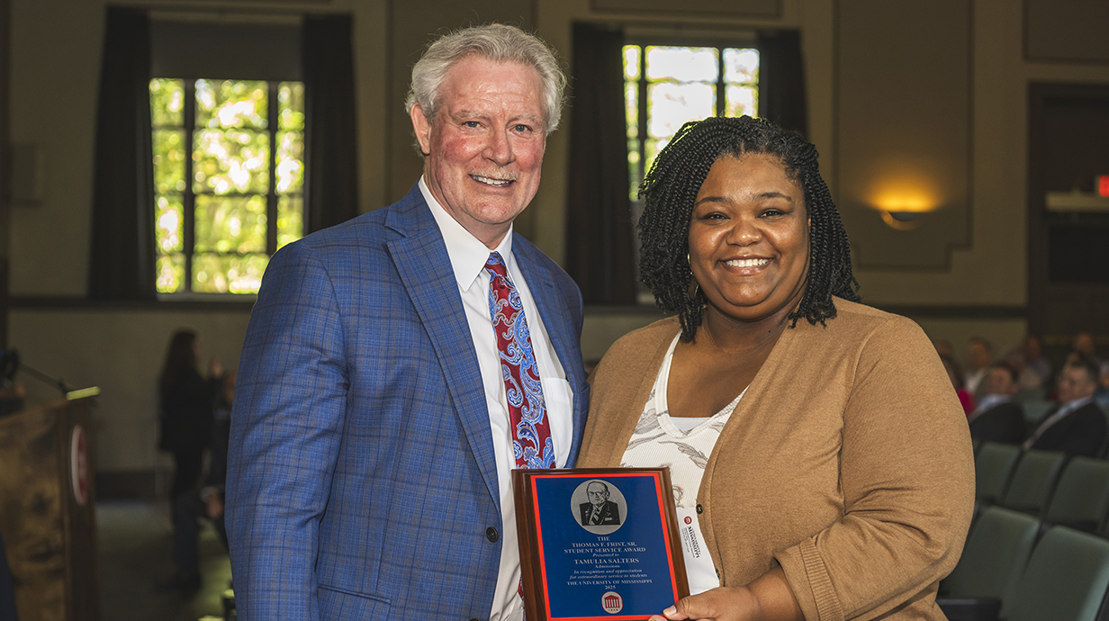 A man presents a plaque to a woman in an auditorium.