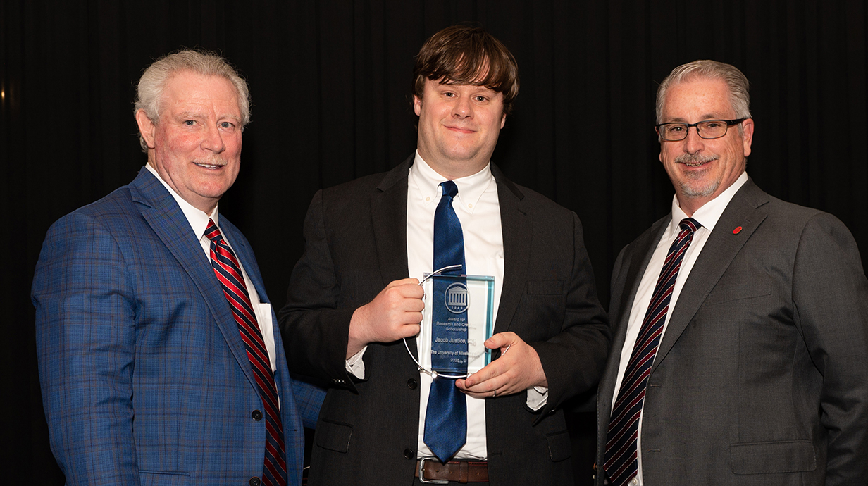 Two men present a trophy to a third man.