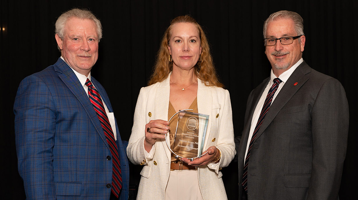 Two men present a trophy to a woman.