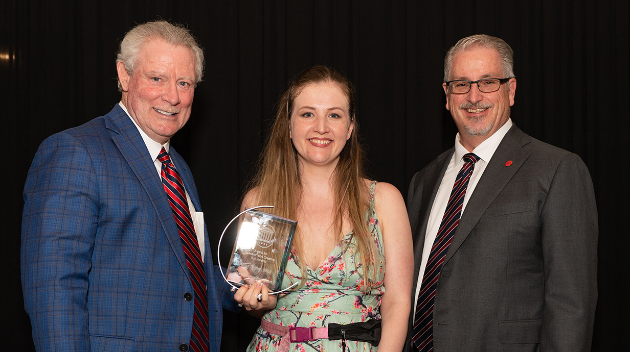 Two men present a trophy to a woman.