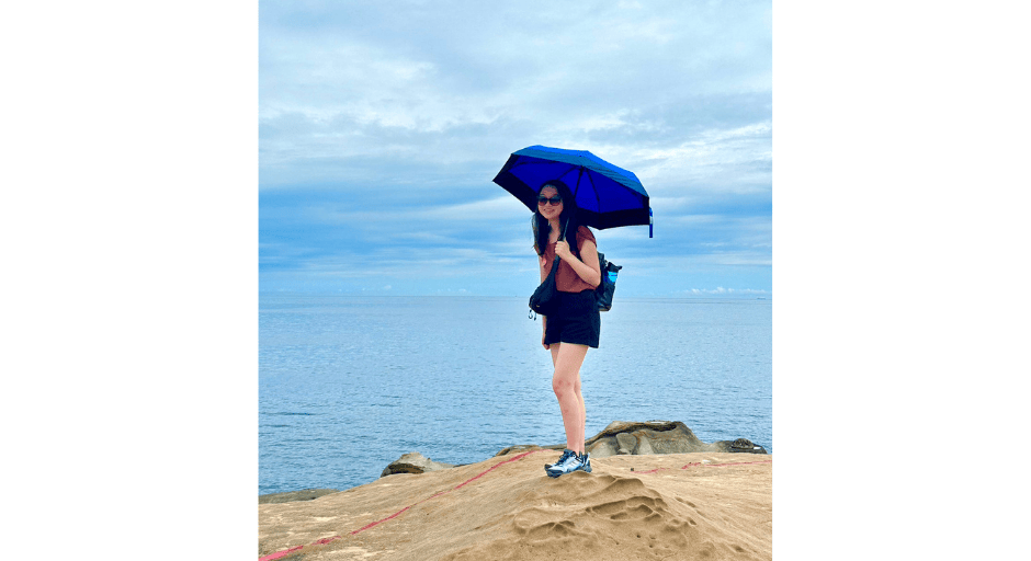 Abigail Moeller at the Yehliu Geopark in New Taipei City, Taiwan holding an umbrella with water in the background.
