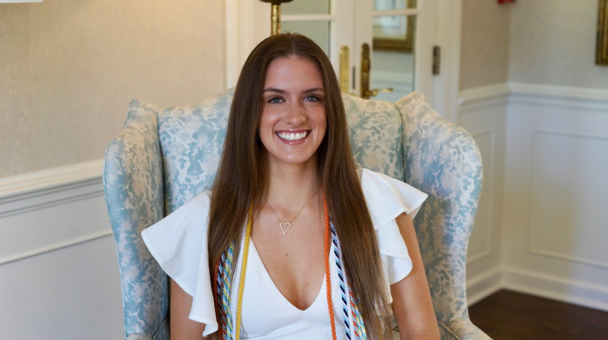 An image of Anna Owens sitting in a chair with graduation cords draped around her.