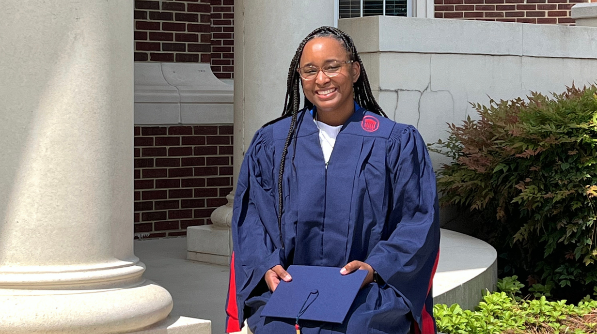 Image of Brandi Williams holding her graduation cap while sitting down in her graduation gown/