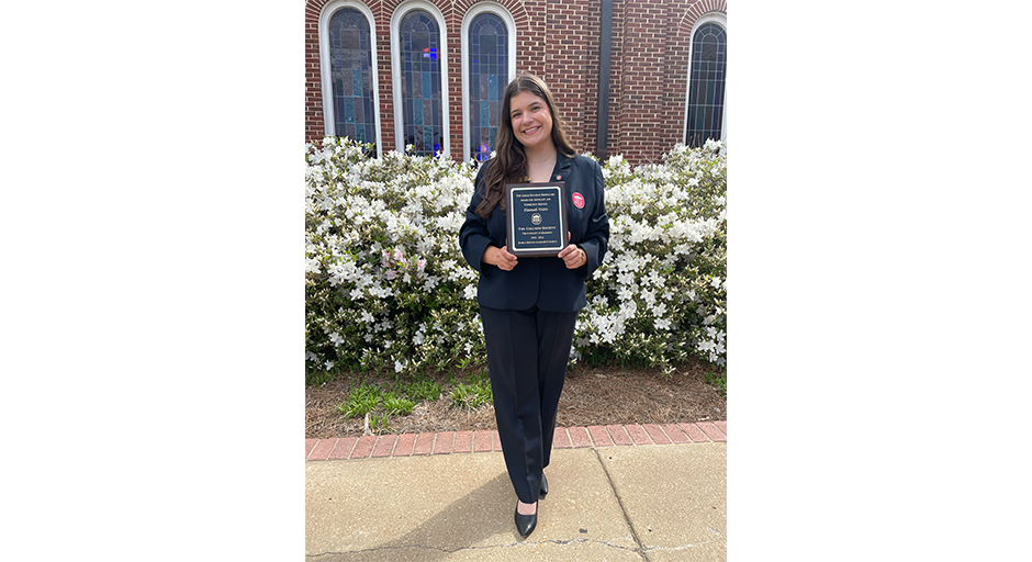 Hannah Watts stands in front of white azaleas holding a plaque.