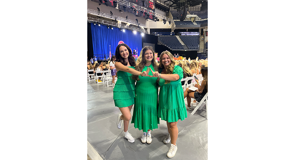 Three women in green dresses and white tennis shoes taking a photo together.