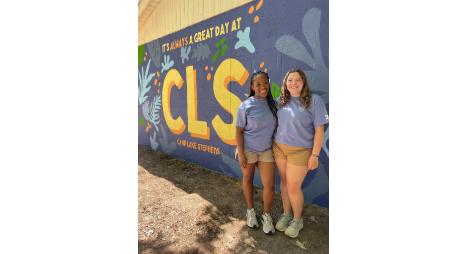 An image of Janelle Minor and Camille Boles in front a mural painting that says "It's always a great day at CLS, Camp Lake Stephens".