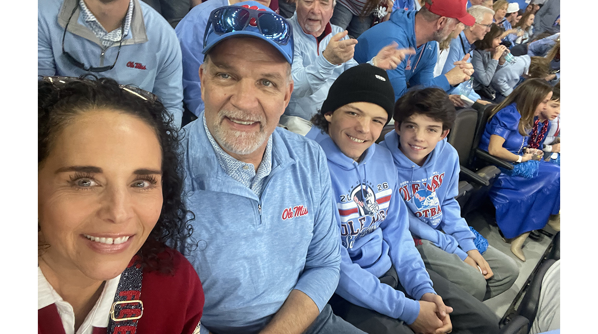 A woman, a man and two boys sit in a sports arena.