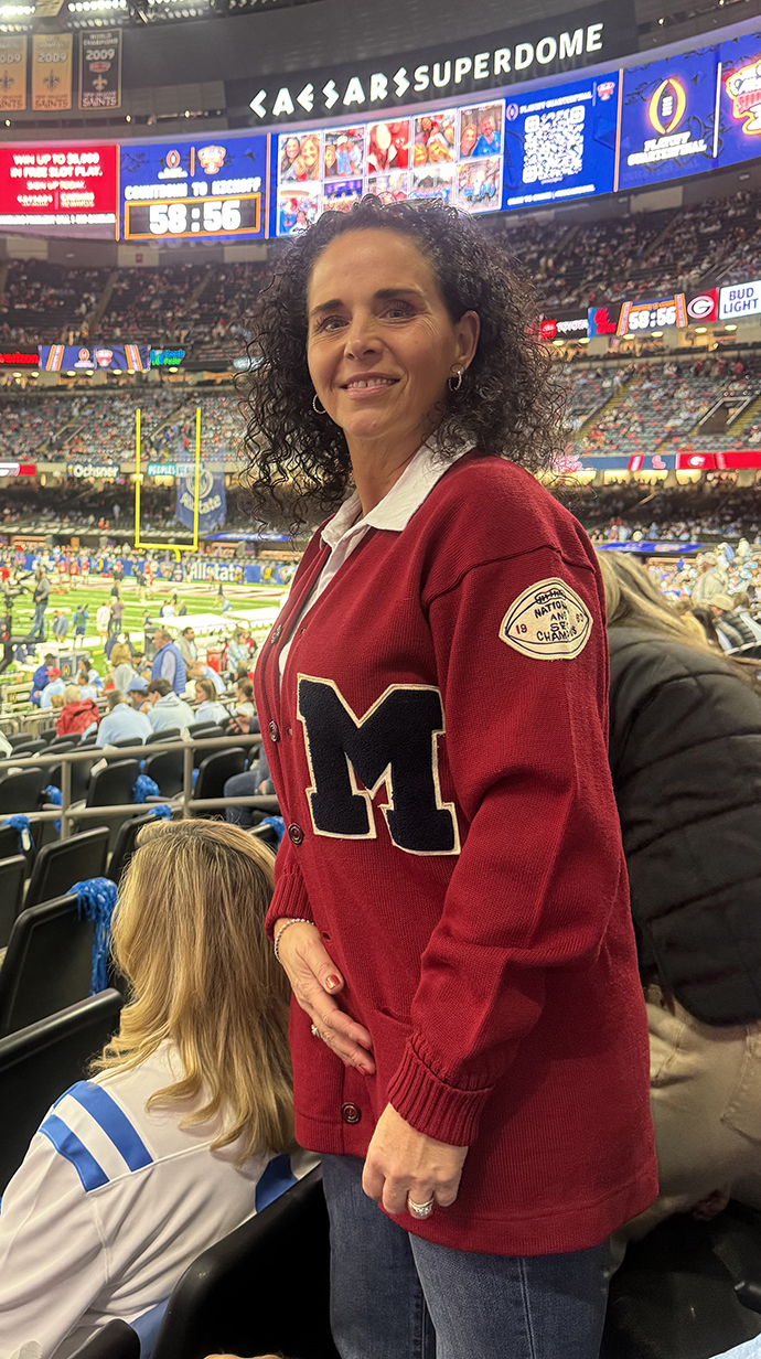 A woman wears a red letterman sweater in a domed sports arena.