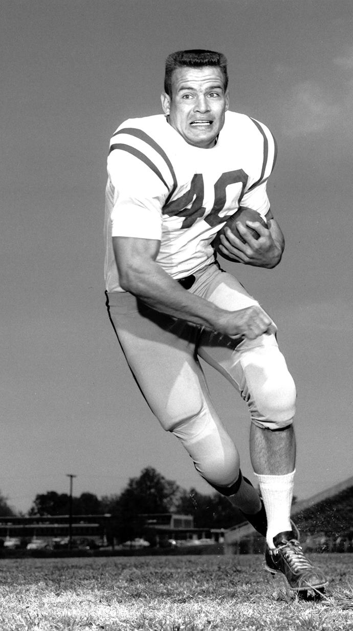 Black-and-white photograph of a football player carrying a football as he runs toward the camera.