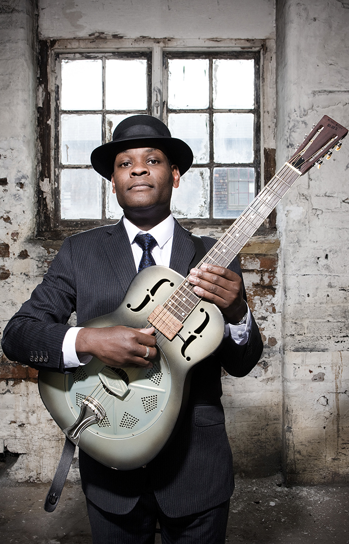 A man wearing a hat holds a resonator guitar.