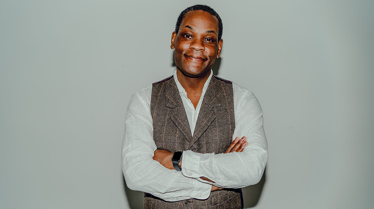 A man wearing a vest over a white shirt stands with his arms crossed.
