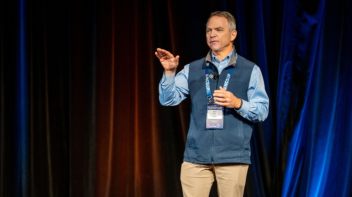A man gestures as he talks on a stage.