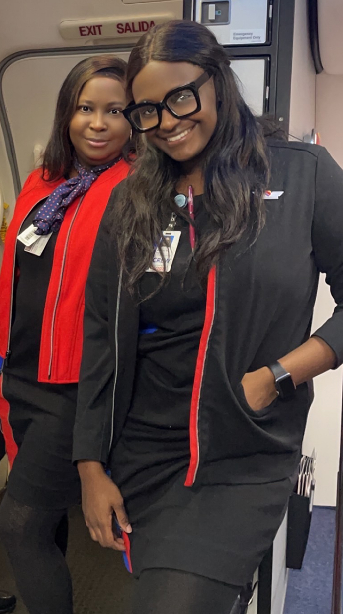 Two women stands in the doorway of a commercial airliner.