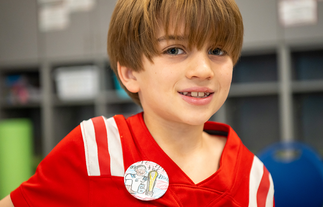 A boy wearing a red football jersey shows off a hand-drawn button for Ole Miss football.