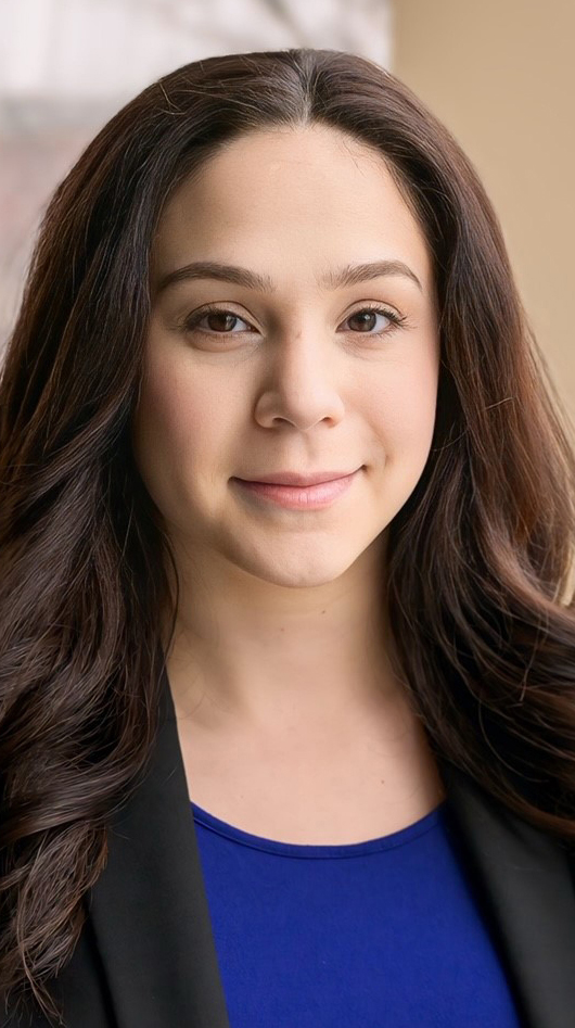 Headshot of a woman wearing a black jacket over a purple blouse.