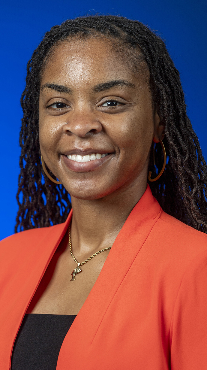 A woman wears a coral-colored jacket over a black blouse.