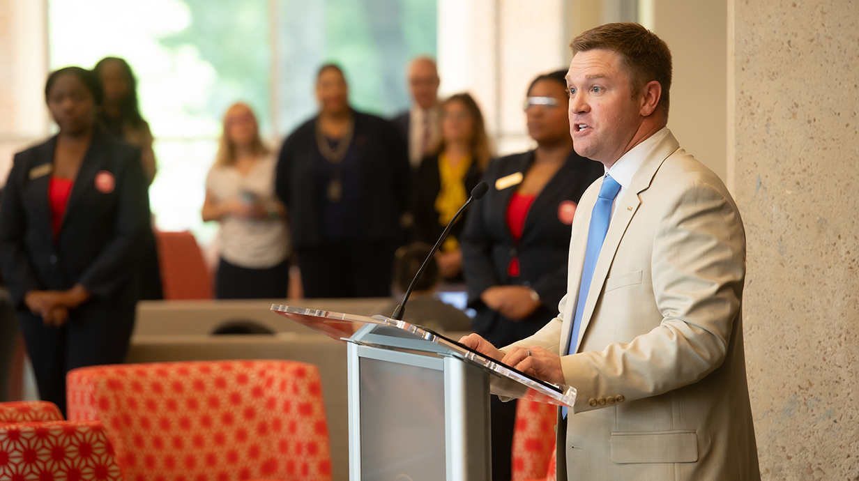 A man wearing a tan suit speaks at a podium.