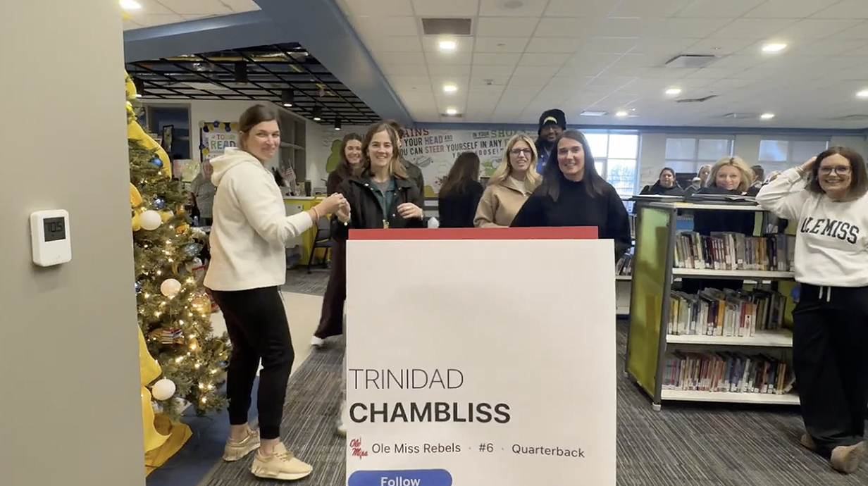 Several men and women look at a photo card of Trinidad Chambliss in a library.
