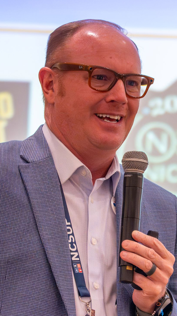 A man wearing a suit talks into a microphone.