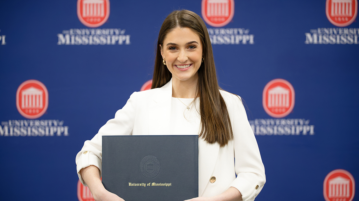 A young woman holds a blue award folder reading 'University of Mississippi.'