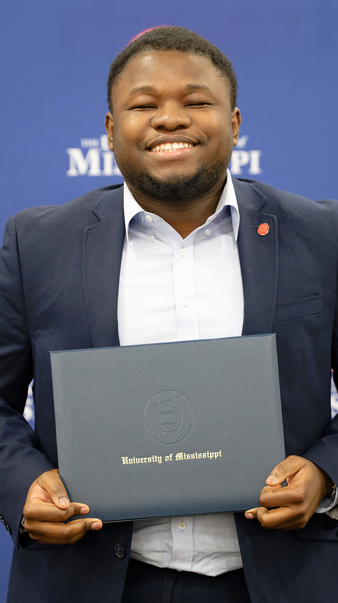 A young man holds a blue award folder reading 'University of Mississippi.'