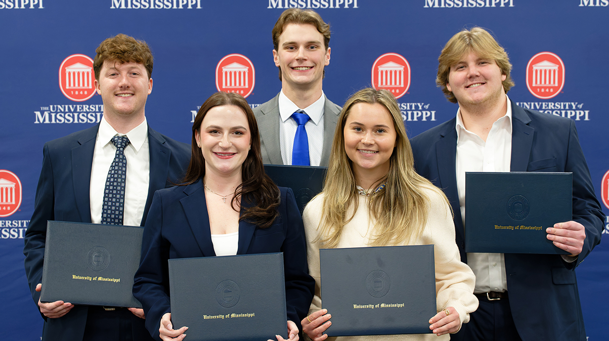 Two young women and three young men, all dressed in business attire, hold blue award folders.