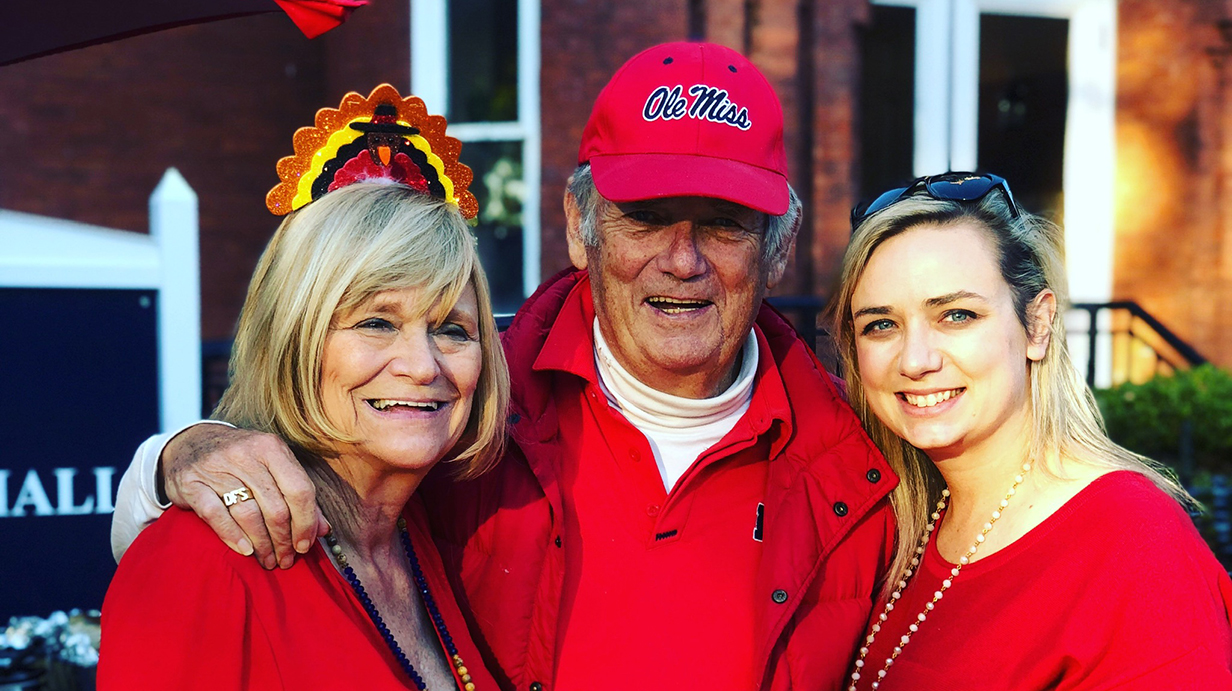 A man and two women, all dressed in red Ole Miss attire, pose for a photo together outdoors.