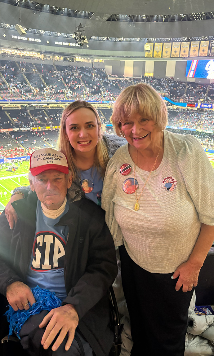 A man in a wheelchair and two women attend a football game in a giant indoor stadium.