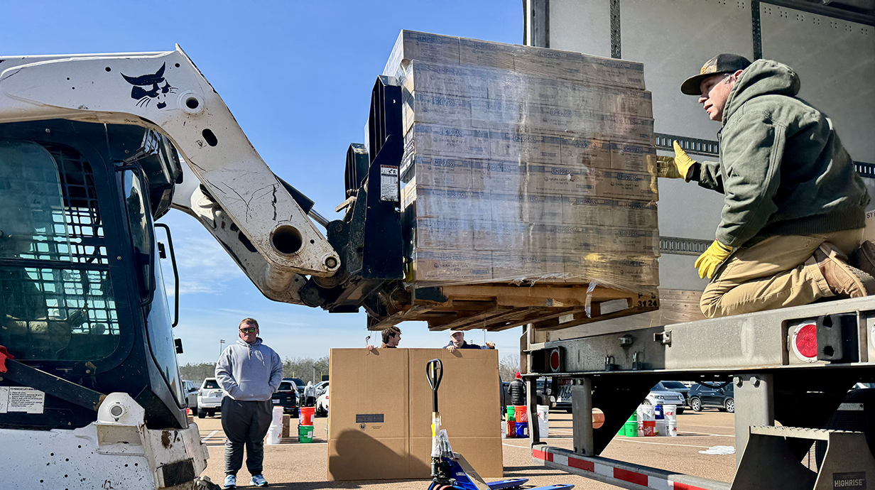 A man guides a palate of boxes on a forklift into the back of a box truck.