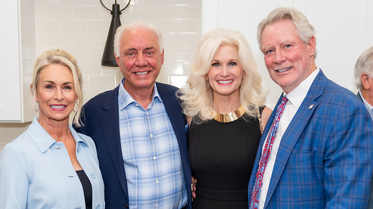 Two men and two women pose for a photo together in a kitchen.