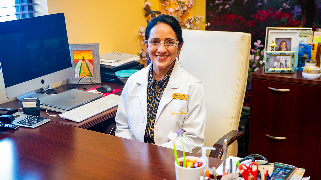 A woman wearing a physician's white coat sits at a desk.
