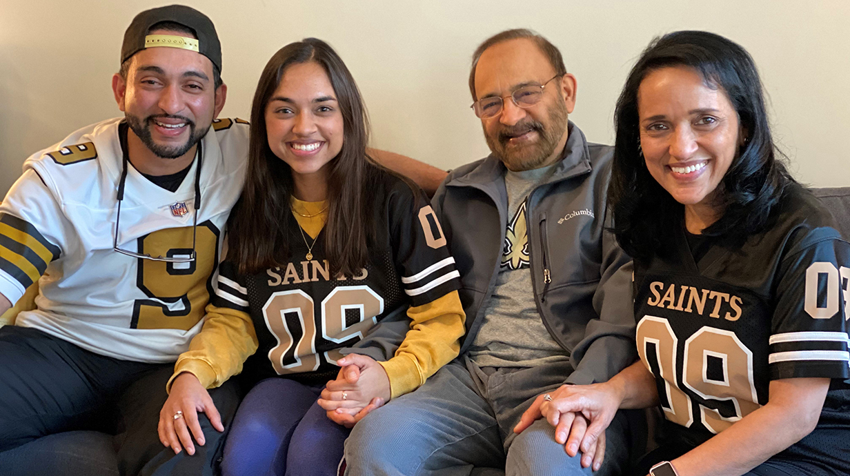 Two men and two women, all wearing New Orleans saints apparel, sit together on a sofa.