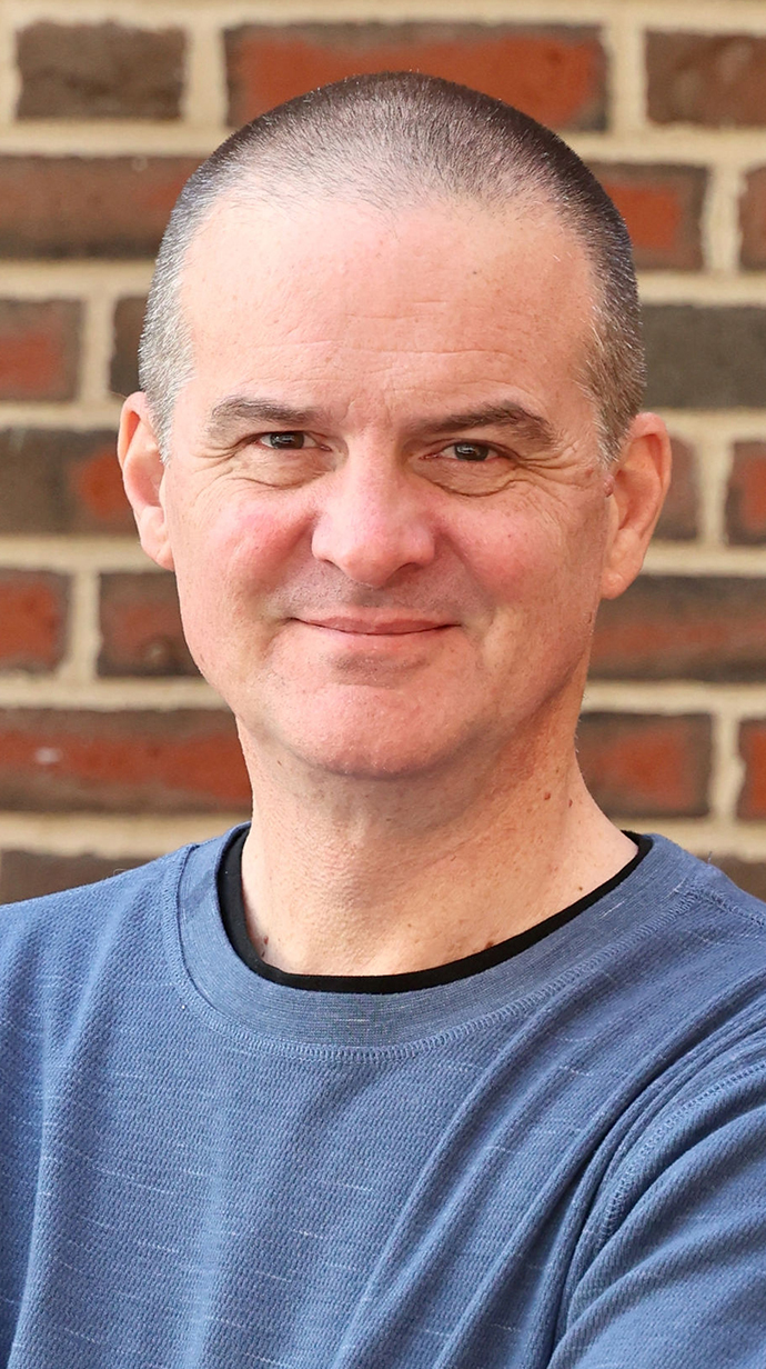 Headshot of a man wearing a blue-gray sweatshirt over a black T-shirt.