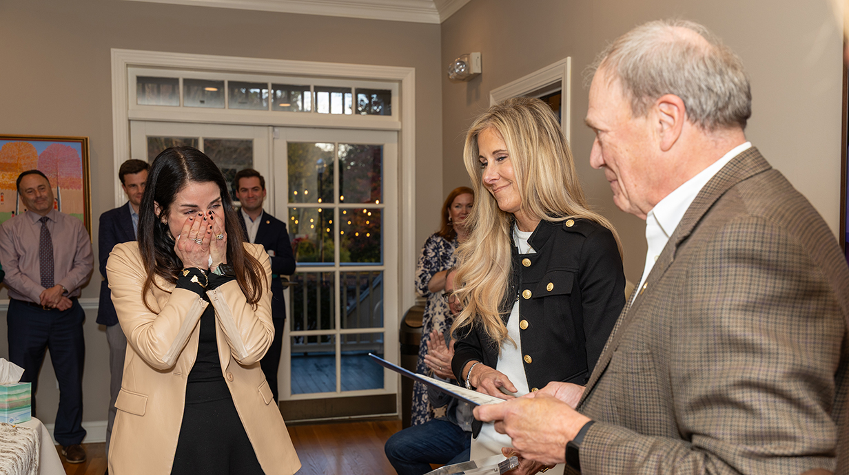 A woman reacts with surprise as another woman and a man present her with a certificate.