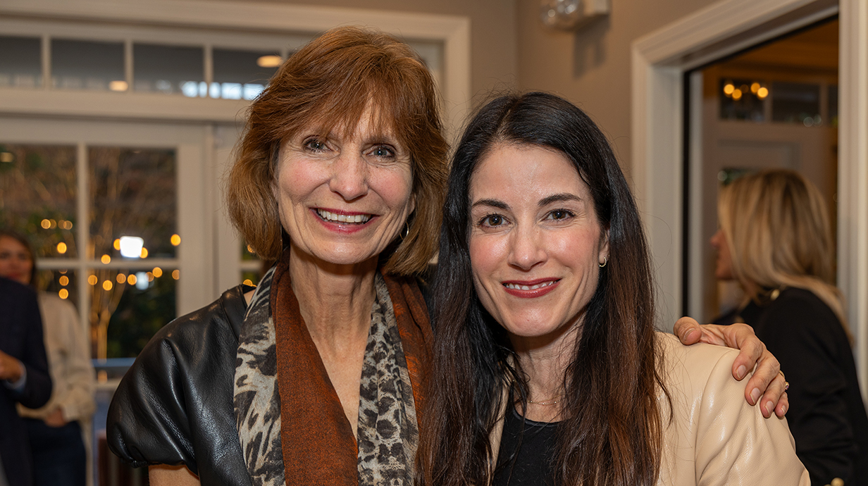 Two women pose for a photo together in a crowded room.