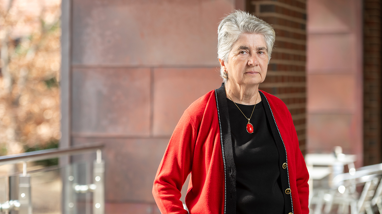A woman wearing a red jacket over a black top stands in an outdoor seating area.