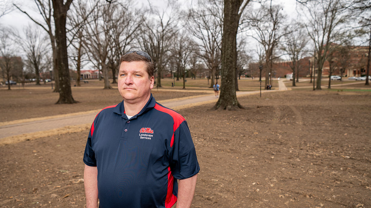 A man wearing a red and blue Ole Miss polo shirt looks over a wooded park.