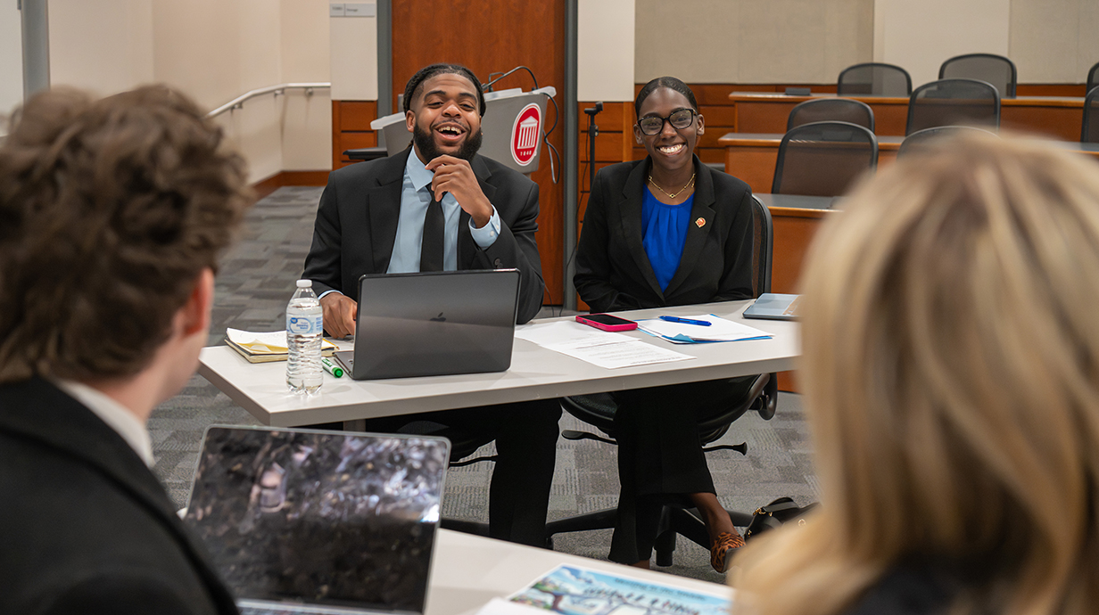 A young man and woman sit at a table facing another young man and woman with their backs to the camera.