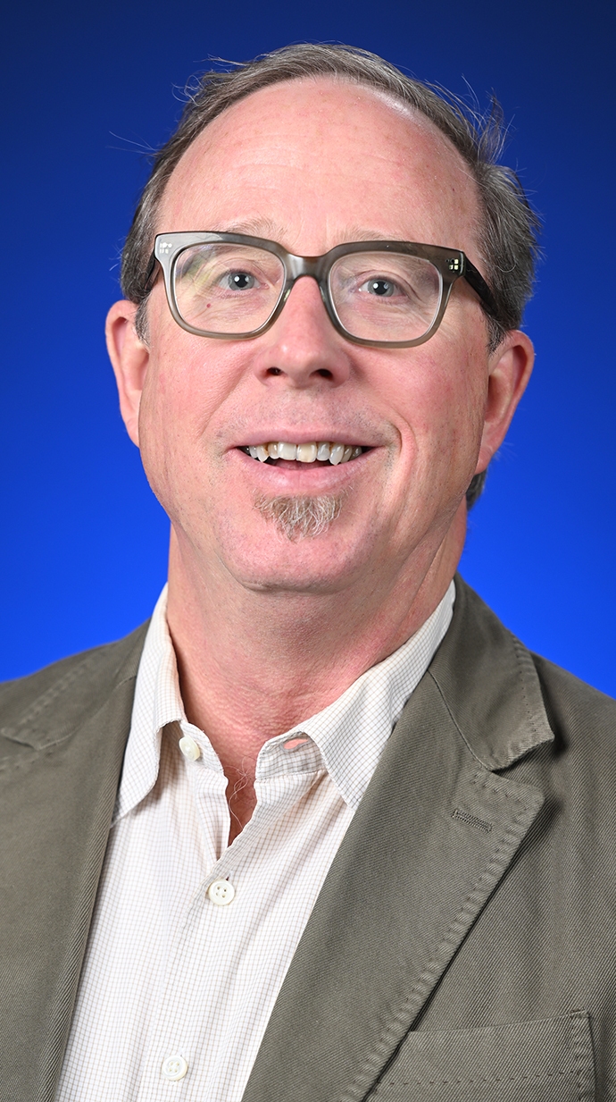 Headshot of a man wearing a gray jacket over a white shirt.