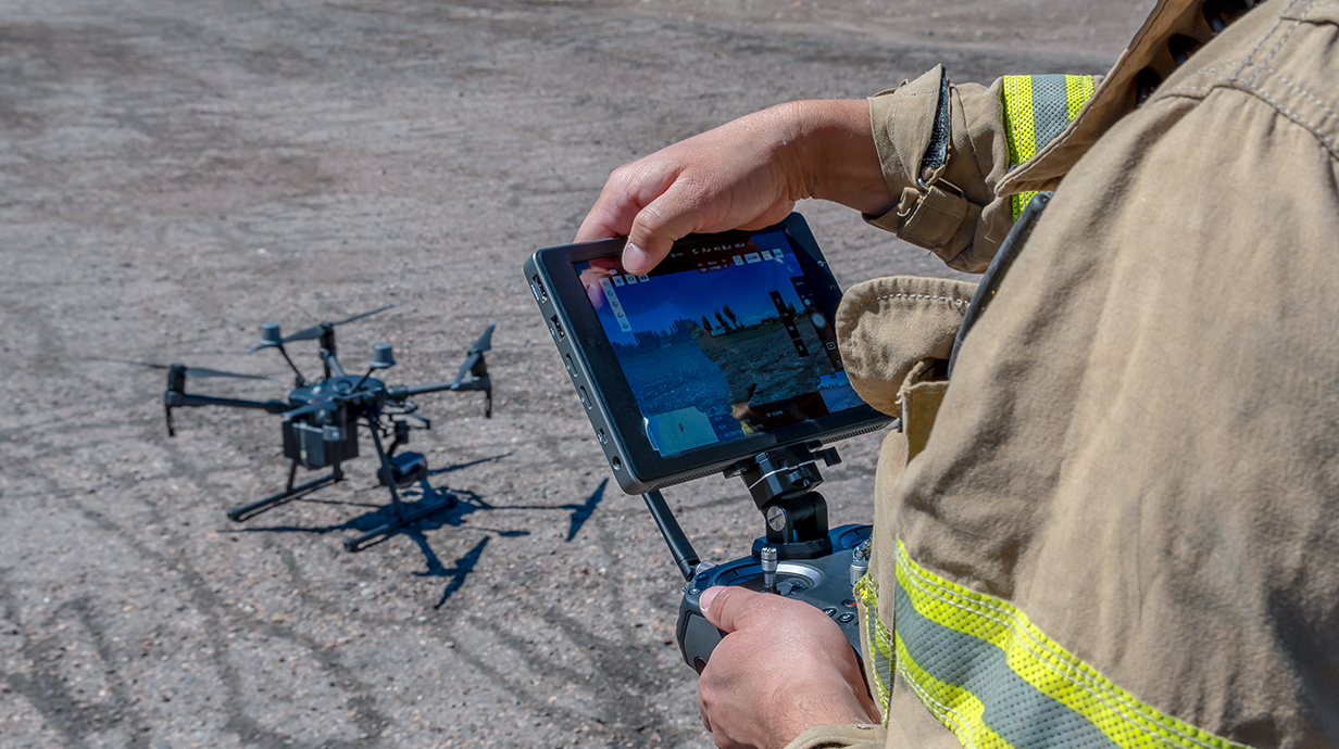 A person wearing a firefighter's canvas jacket operates controls for a drone.