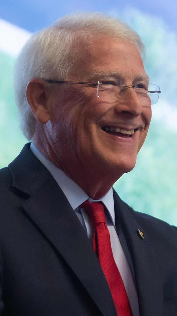 Headshot of a man wearing a suit in front of a projection screen.